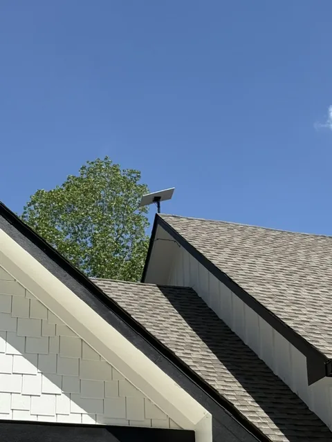 Starlink mounted high on a shingle roof ridge against a deep blue sky.