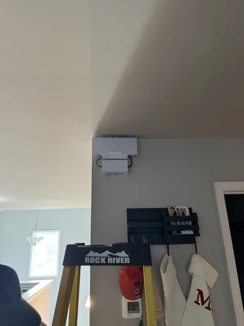 White Starlink unit mounted high on a wall where it meets a vaulted ceiling, with the cable run inside the wall.