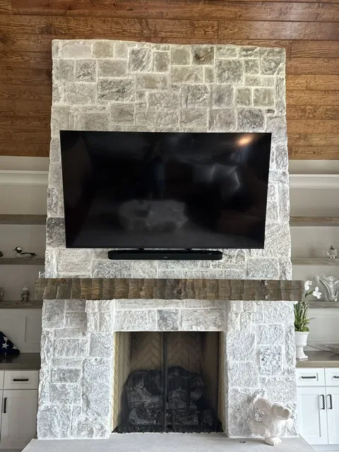 Large flat screen television and soundbar mounted flush on a white stone fireplace surround with a timber mantel.